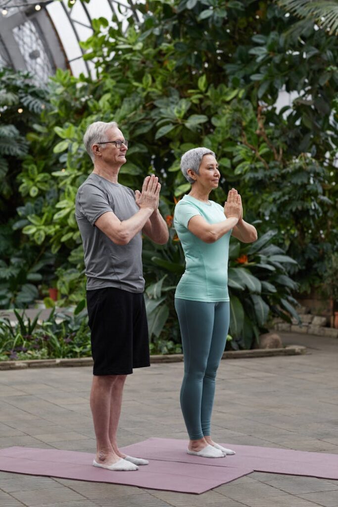 pexels photo 6787498 Senior couple practicing yoga poses together in a lush greenhouse setting.